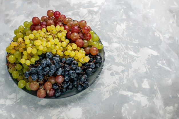 Vista frontal uvas frescas frutas jugosas y suaves dentro de la placa sobre superficie blanca