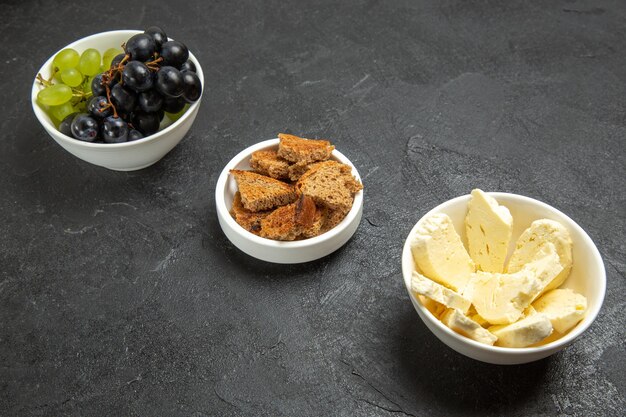 Vista frontal de uvas frescas con queso blanco y pan oscuro en rodajas sobre el fondo oscuro, comida, plato, leche, fruta