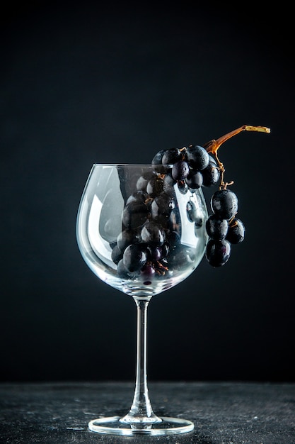 Vista frontal de uvas negras en copa de vino en el espacio libre de la mesa negra