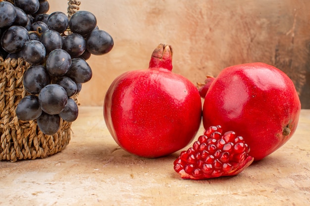 Vista frontal uvas negras frescas con granadas en el fondo claro vino de fruta madura suave