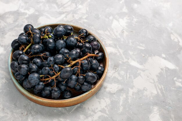 Vista frontal de uvas negras frescas jugosas frutas dulces suaves en el escritorio blanco claro frutas vino de jugo suave fresco