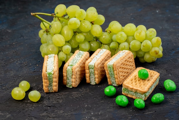 Foto gratuita una vista frontal de las uvas verdes frescas agrias jugosas y suaves con galletas en el fondo oscuro fruta verde planta madura