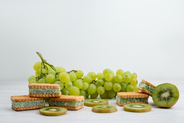 Una vista frontal de las uvas verdes frescas agrias jugosas y suaves con galletas y kiwis en el fondo blanco fruta verde planta madura