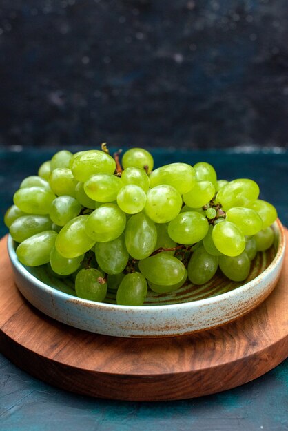 Vista frontal uvas verdes frescas frutas jugosas suaves dentro de la placa en el escritorio azul oscuro.