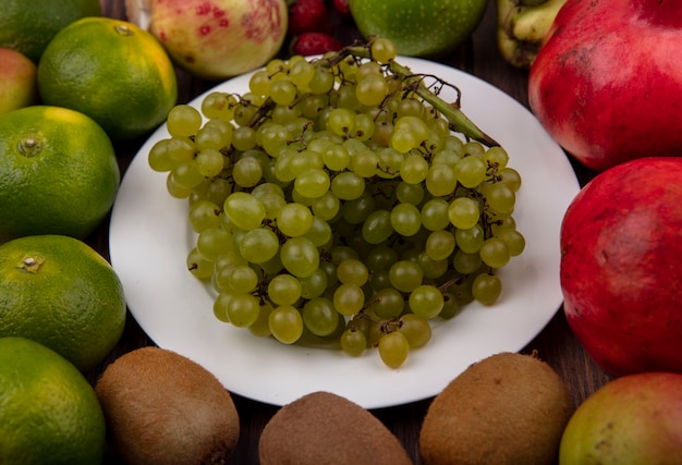 Vista frontal de uvas verdes en un plato con kiwi, mandarinas y granadas