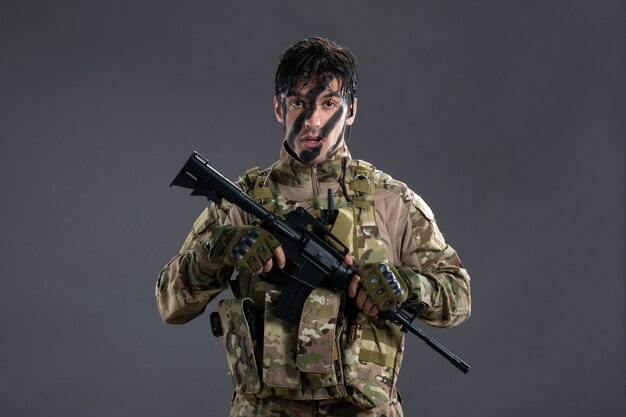 Vista frontal del valiente soldado luchando en camuflaje con ametralladora en pared gris