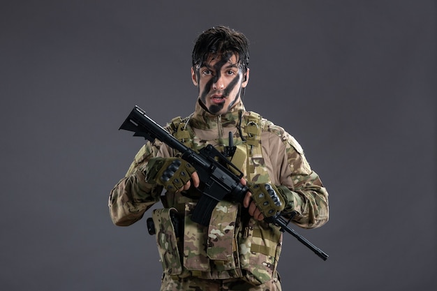Vista frontal del valiente soldado luchando en camuflaje con ametralladora en pared gris