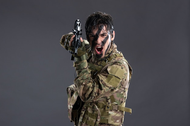 Vista frontal valiente soldado luchando en camuflaje con ametralladora pared oscura