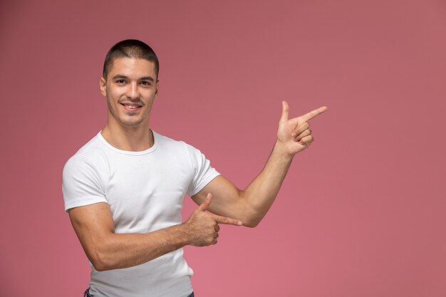 Vista frontal del varón joven en camisa blanca posando con expresión señalando sobre fondo rosa