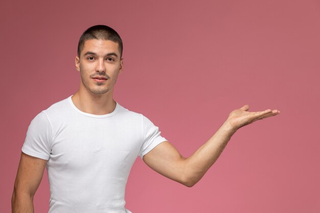 Vista frontal del varón joven con camisa blanca posando con su mano sobre fondo rosa