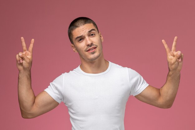 Vista frontal del varón joven con camisa blanca que muestra signos de victoria sobre fondo rosa