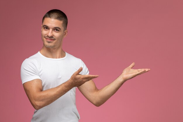 Vista frontal del varón joven en camisa blanca sonriendo y posando sobre fondo rosa