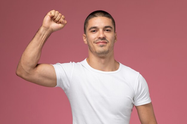 Vista frontal del varón joven en camisa blanca sonriendo y regocijándose en el fondo rosa