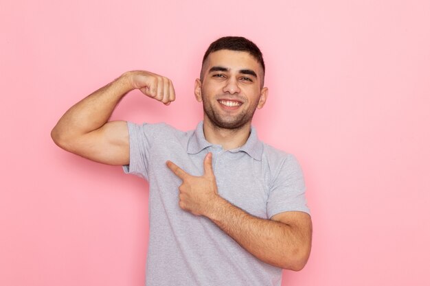 Vista frontal del varón joven en camisa gris posando y sonriendo con flexión en rosa