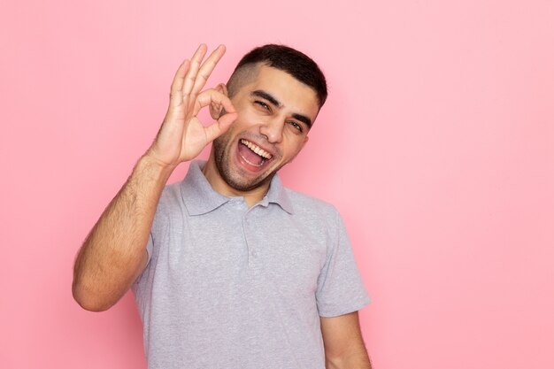 Vista frontal del varón joven en camisa gris posando y sonriendo mostrando bien firmar en rosa