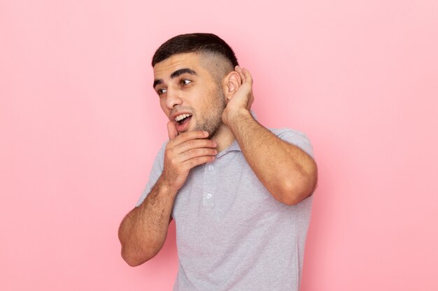 Vista frontal del varón joven en camisa gris tratando de escuchar con expresión de sorpresa en rosa