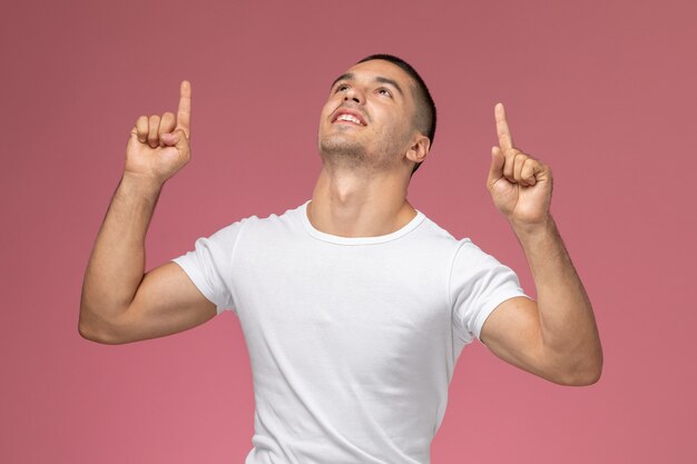 Vista frontal del varón joven en camiseta blanca regocijándose y agradeciendo a Dios sobre fondo rosa