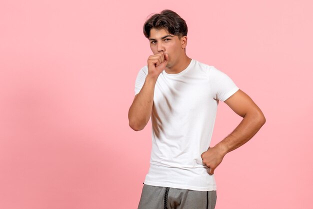 Vista frontal del varón joven en camiseta blanca tosiendo sobre fondo rosa