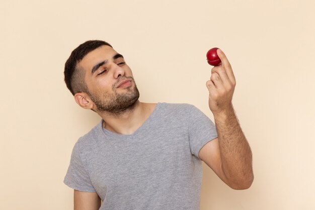 Vista frontal del varón joven en camiseta gris y jeans con ciruela roja amarga en beige