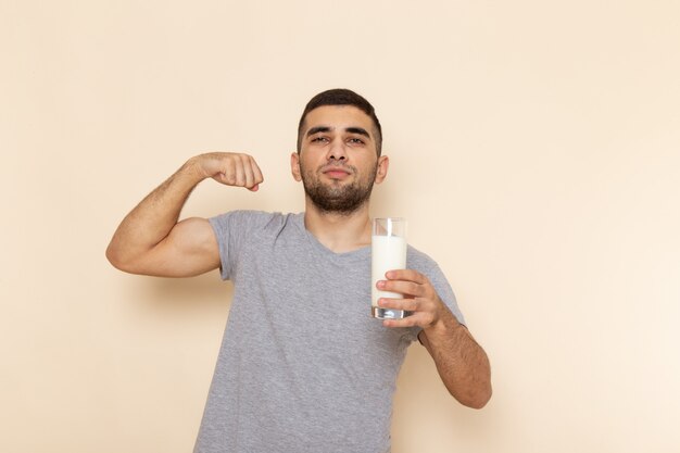 Vista frontal del varón joven en camiseta gris con vaso de leche en beige