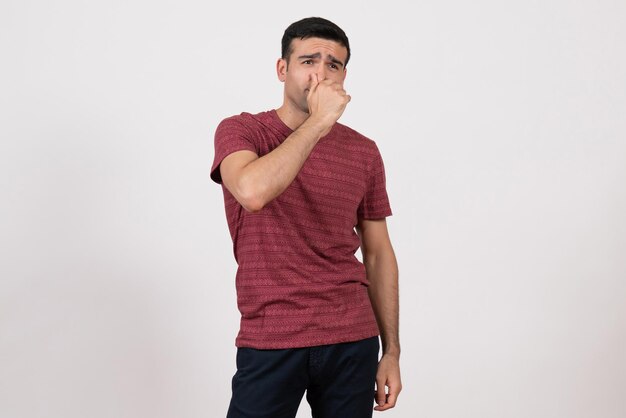 Vista frontal del varón joven en camiseta posando cerrando la nariz sobre fondo blanco.