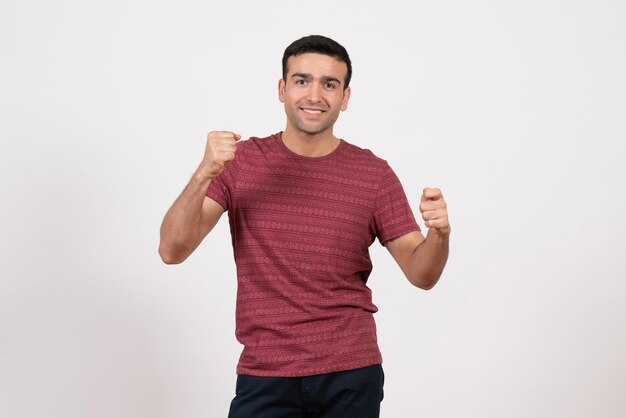 Vista frontal del varón joven en camiseta posando y regocijándose sobre fondo blanco.