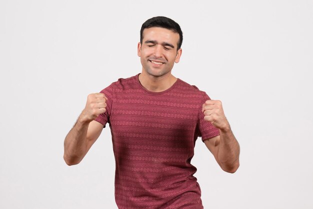 Vista frontal del varón joven en camiseta roja oscura posando y regocijándose sobre fondo blanco.