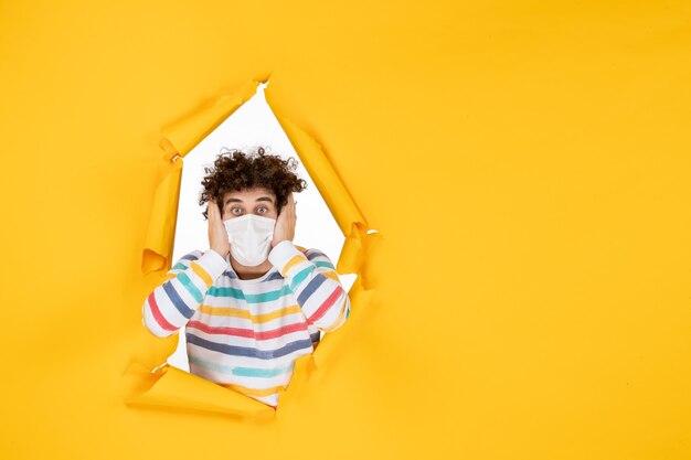 Vista frontal del varón joven en máscara estéril en color amarillo covid- virus de la pandemia de salud