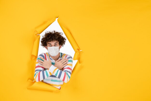 Vista frontal del varón joven en máscara estéril en color amarillo salud foto covid-virus pandémico humano