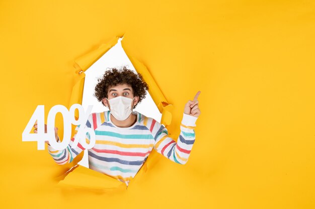 Vista frontal del varón joven en la máscara que sostiene la escritura en el color amarillo de la pandemia del virus que compra la venta de la foto de la salud