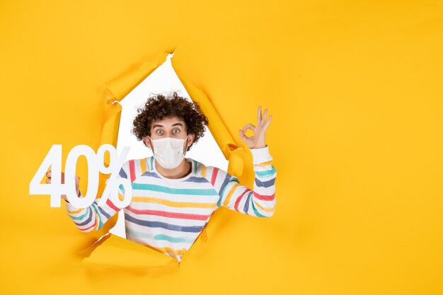 Vista frontal del varón joven en la máscara que sostiene la escritura sobre los colores de la pandemia del virus amarillo salud covid venta de fotos