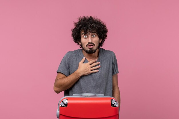 Vista frontal del varón joven preparándose para las vacaciones con la bolsa en el escritorio rosa