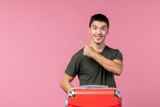 Vista frontal del varón joven preparándose para las vacaciones con una bolsa grande en el espacio de color rosa claro