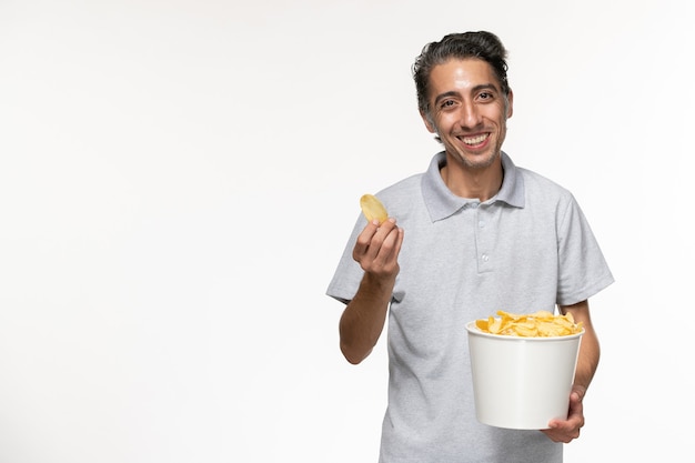 Vista frontal del varón joven que sostiene la cesta con papas fritas en la superficie blanca clara