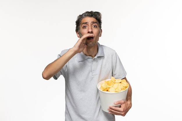 Vista frontal del varón joven que sostiene la cesta con papas fritas en la superficie blanca clara