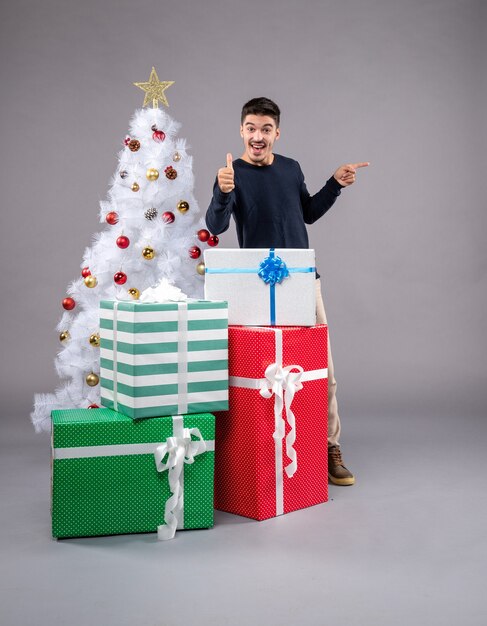 Vista frontal del varón joven con regalos de Navidad en el escritorio de luz vacaciones de año nuevo de Navidad