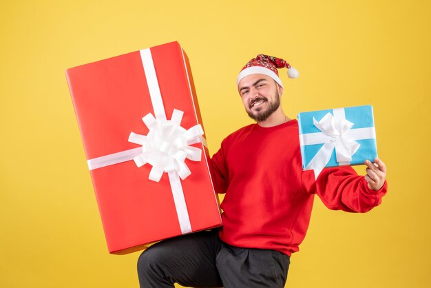 Vista frontal del varón joven con regalos de Navidad sobre fondo amarillo