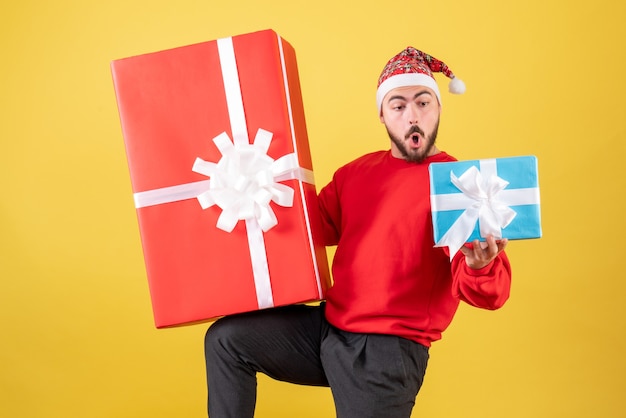 Vista frontal del varón joven con regalos de Navidad sobre fondo amarillo