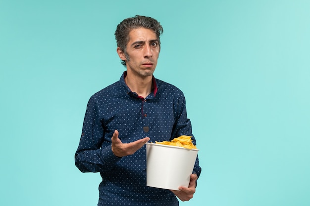 Vista frontal varón de mediana edad sosteniendo la cesta con patatas cips en el escritorio azul