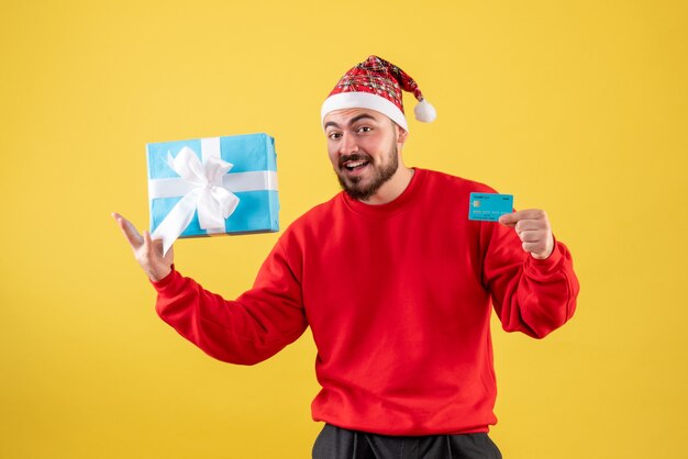 Vista frontal de los varones jóvenes con regalo de Navidad y tarjeta bancaria sobre fondo amarillo