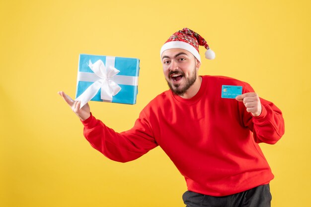 Vista frontal de los varones jóvenes con regalo de Navidad y tarjeta bancaria sobre fondo amarillo