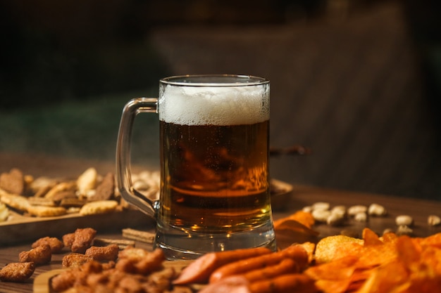 Vista frontal vaso de cerveza con cerveza bocadillos picatostes patatas fritas y salchichas en la mesa