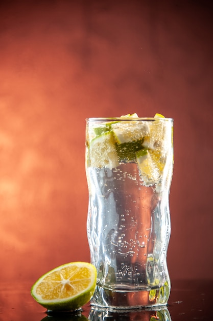 Vista frontal de un vaso de refresco con rodajas de limón en una foto de color rosa claro, agua de champán, bebida de cóctel, limonada