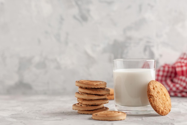 Vista frontal del vaso de vidrio lleno de leche y galletas, toalla roja pelada en el lado izquierdo sobre fondo blanco manchado