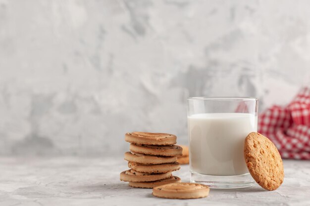 Vista frontal del vaso de vidrio lleno de leche y galletas, toalla roja pelada en el lado izquierdo sobre fondo blanco manchado