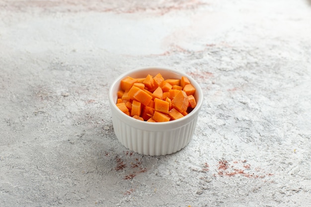 Vista frontal de vegetales de naranja en rodajas dentro de una olla pequeña sobre superficie blanca