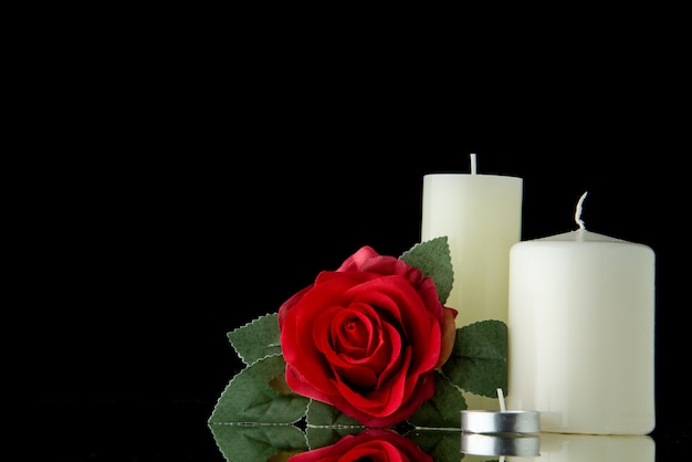 Vista frontal de velas blancas con flor roja sobre pared negra