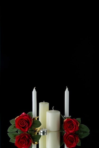 Foto gratuita vista frontal de velas blancas con flores rojas sobre pared negra