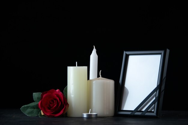 Vista frontal de velas blancas con rosa roja como memoria en la pared oscura