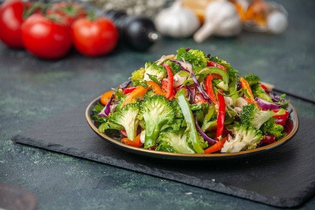 Vista frontal de verduras frescas, flor blanca, martillo de madera y deliciosa ensalada vegana sobre fondo de color oscuro